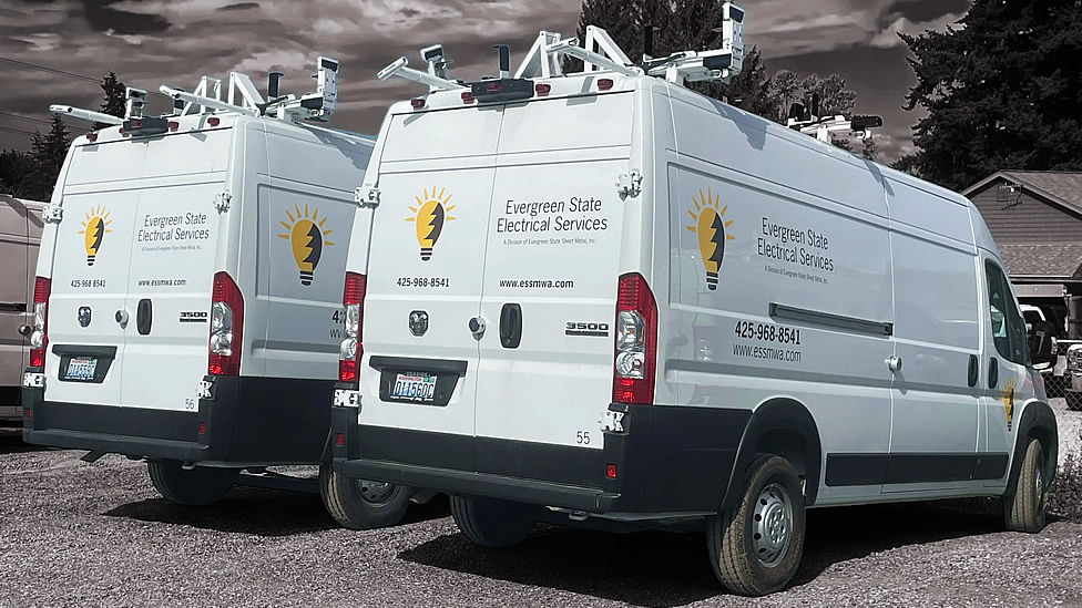 Two white Evergreen State Electrical Services vans are parked side by side in a lot, each with company logos, contact information, and ladder racks on their roofs. Evergreen State Heat & AC