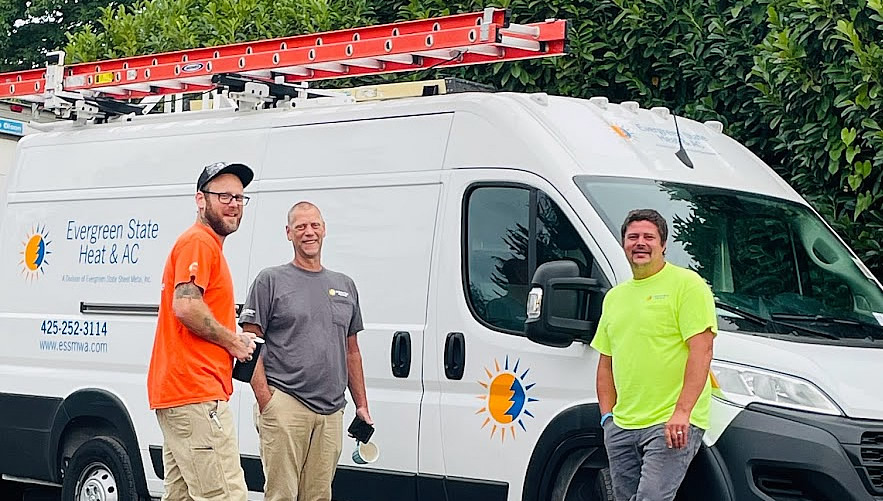 Three men stand in front of an Evergreen State Heat & A/C service van with ladders on top, outdoors on a cloudy day. Evergreen State Heat & AC