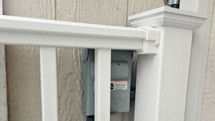 White vinyl railing installed very close to an outdoor electrical box mounted on a wood wall, limiting access to the box. Evergreen State Heat & AC
