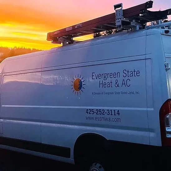 White Evergreen State Heat & AC service van with ladders on top is parked outdoors at sunset, with trees and buildings in the background, highlighting their expertise in affordable plumbing and HVAC solutions. Plumbers in Black Diamond, WA
